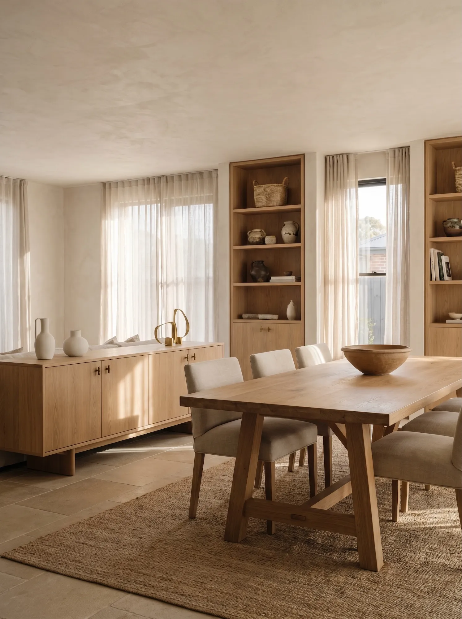 Warm open-plan living and dining room with bespoke oak dining table, low sideboard, and built-in shelving in soft natural light